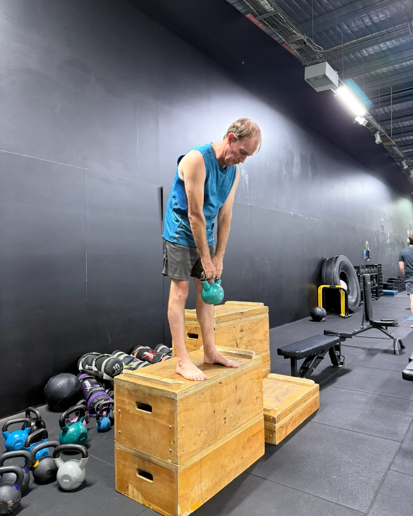A member balanced on a wooden box holding a kettlebell in both hands