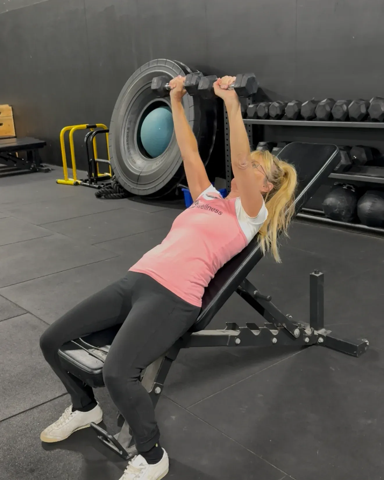A member pressing a dumbbell above her chest on an incline bench