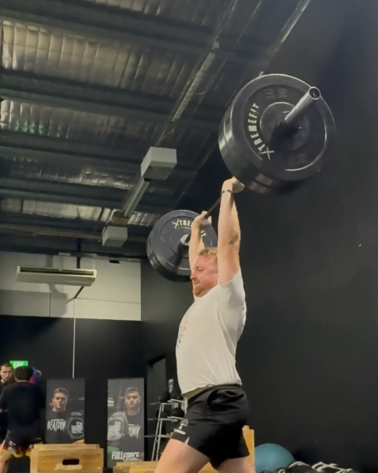 A member locking out a loaded barbell overhead, barefoot