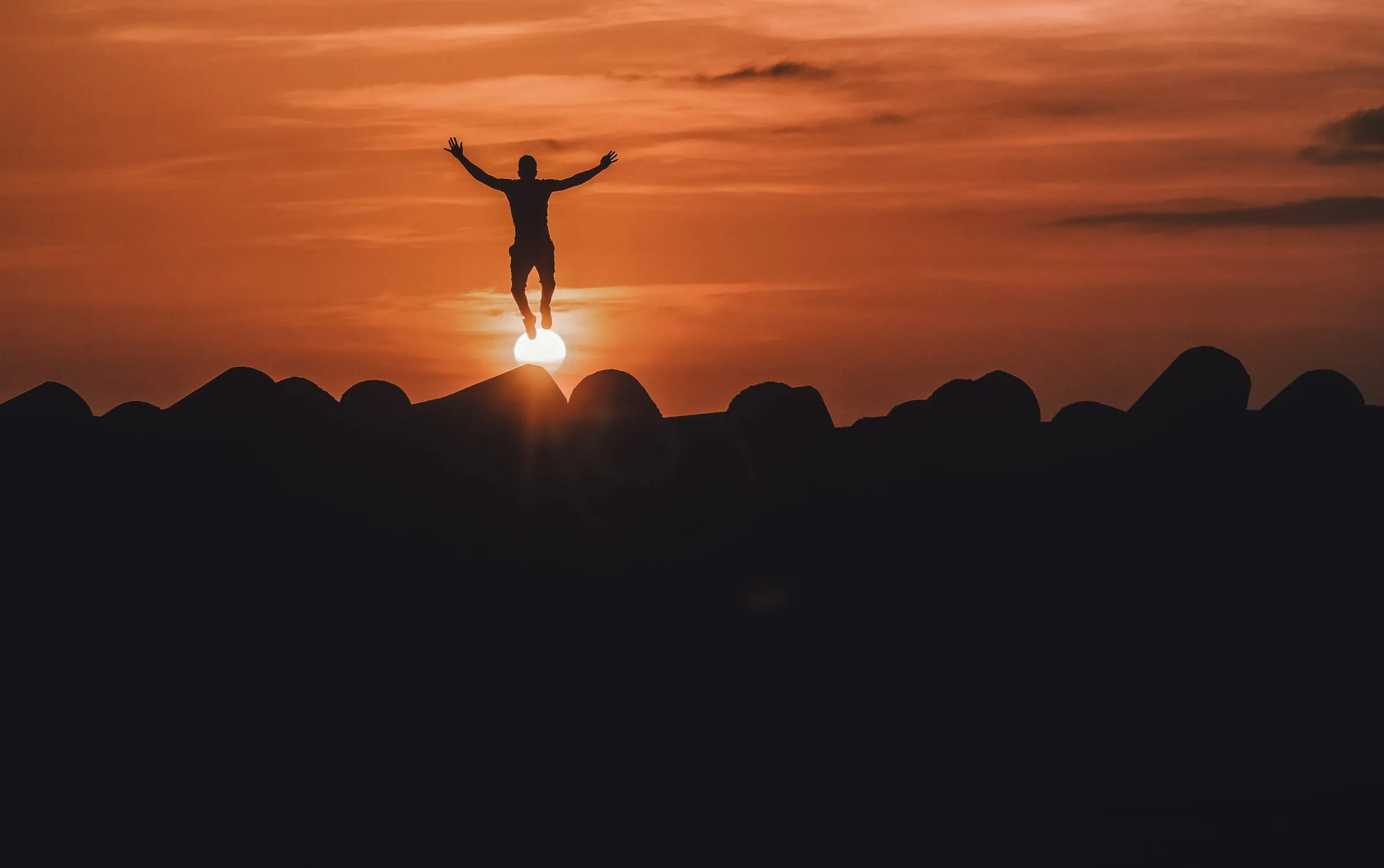 A person standing on a hilltop at sunset with their arms raised