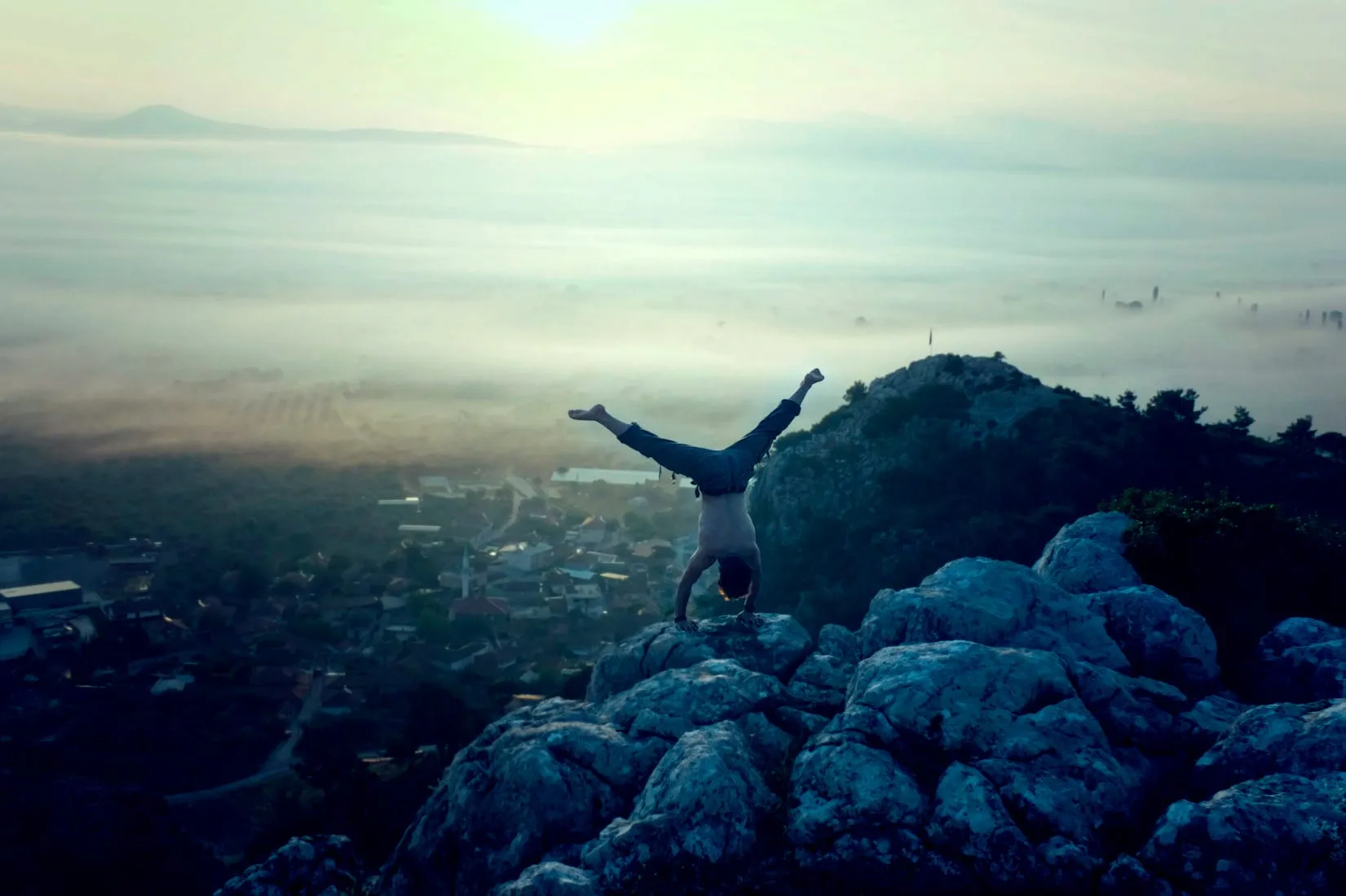 A person doing a handstand on rocks above a valley at dawn